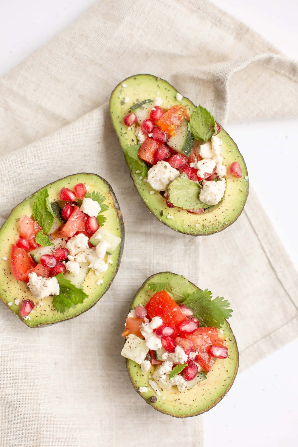 avocado with parsley, tomato, and feta cheese on a tan linen cloth