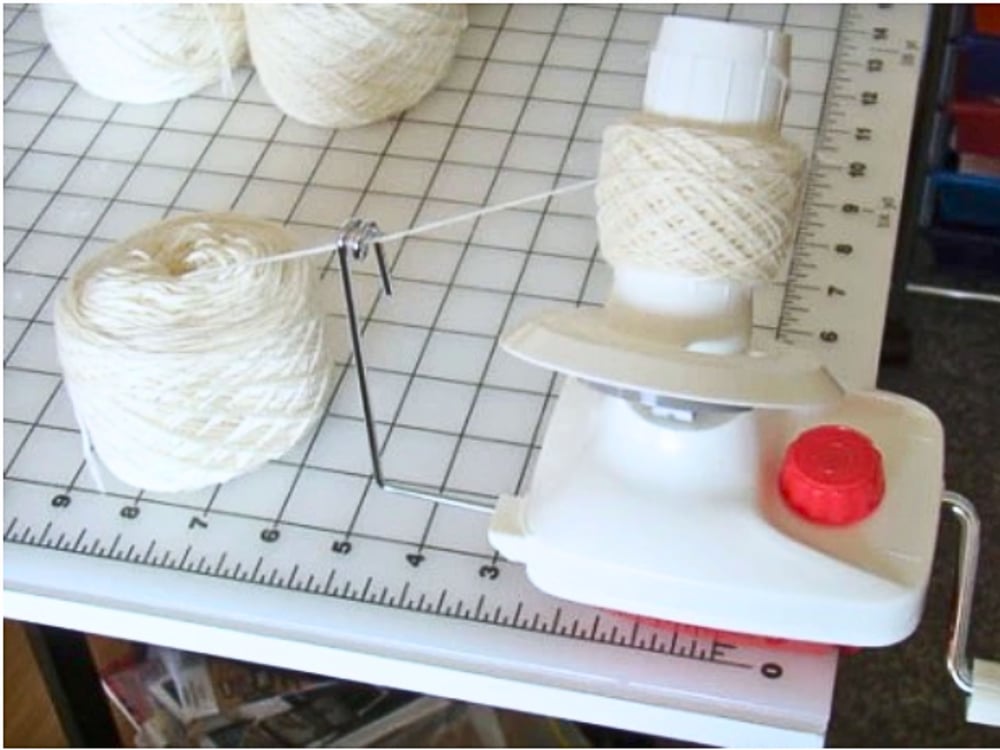 White yarn being wound into a  red and white ball winder that is clamped to a sewing table