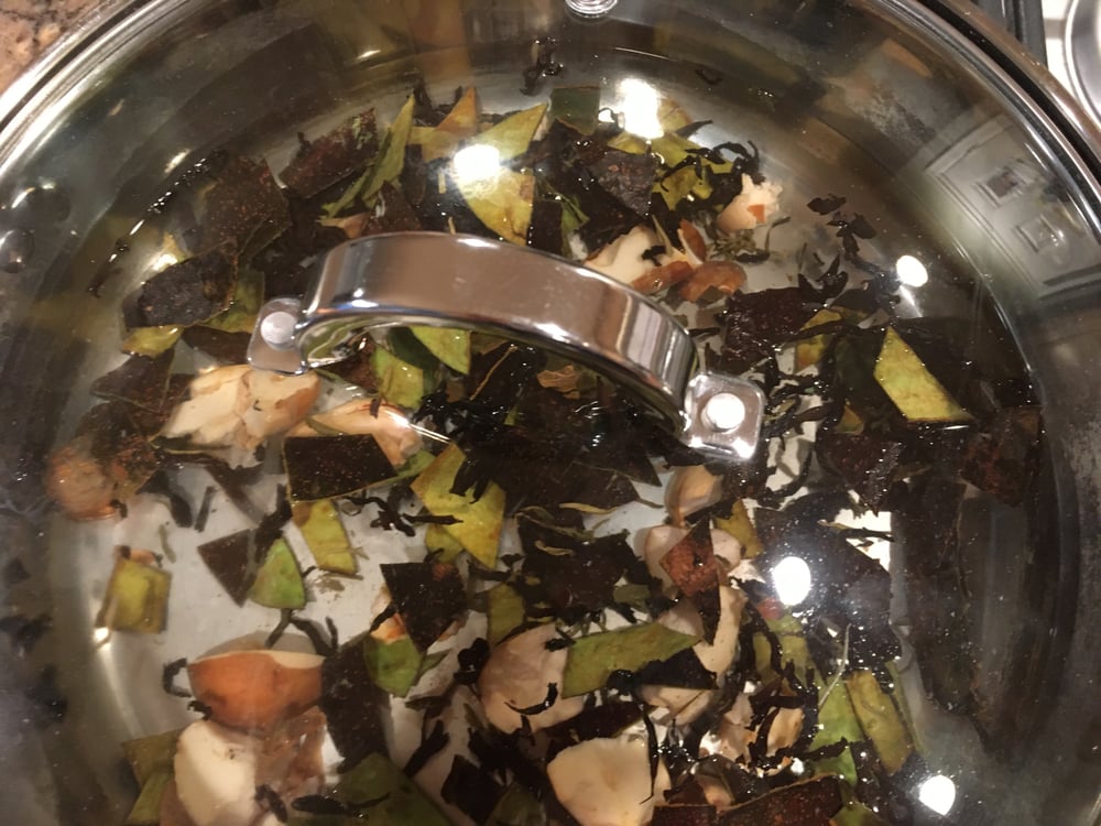 A pot filled with water, avocado pits, and skins simmering together to prepare a natural dye for fabric.