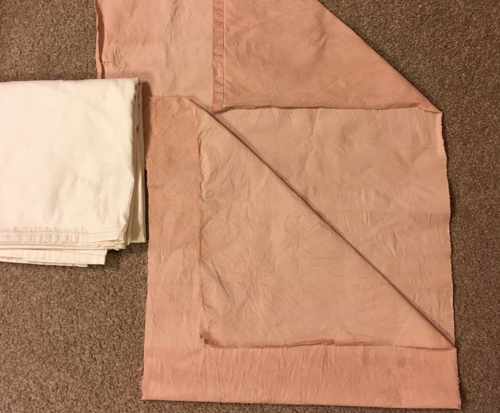A side-by-side comparison of fabric before and after natural dyeing. On the left, the undyed fabric is white and neatly folded. On the right, the dyed fabric lies flat, with top-right and bottom-left corners folded up, revealing slightly darker and lighter colors than the other parts of the fabric.