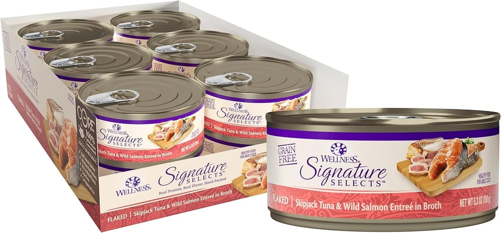 A box of Wellness Signature Selects Grain Free Flaked Skipjack Tuna &amp; Wild Salmon Entrée in Broth maine coon cat food cans, with one can in front and six cans partially visible in the open package behind.