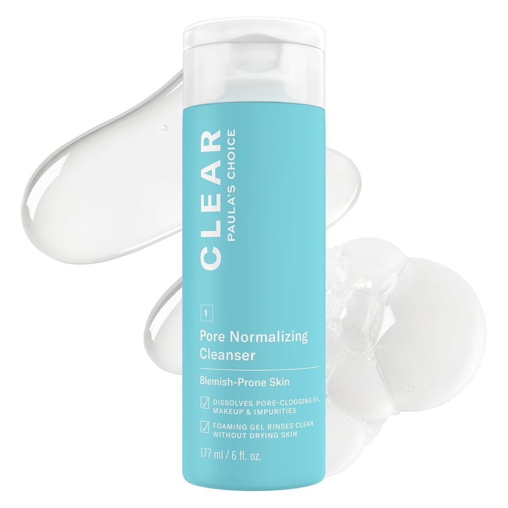A blue bottle of Paula’s Choice CLEAR Pore Normalizing Cleanser with white text stands upright. Behind it, smears and bubbles of clear gel highlight the texture of this salicylic acid formula, labeled for blemish-prone and blackhead-prone skin.
