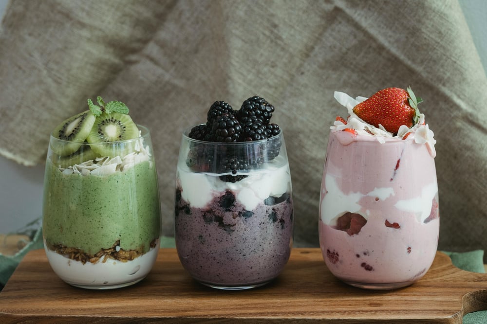 “Three glasses of Greek yogurt parfait topped with fresh kiwis, blackberries, strawberries, and sprinkled chia seeds, a colorful high-protein and antioxidant-rich breakfast idea
