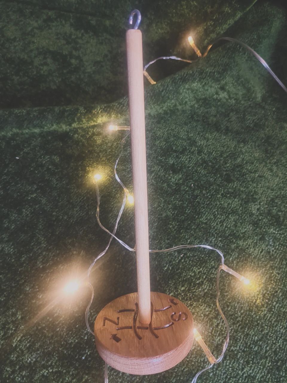 A wooden drop spindle with a hook in the top and a whorl at the bottom. The whorl has been engraved with arrows indicating the direction for S and Z twist yarn, as well as the crossed threads logo of Flaxland.