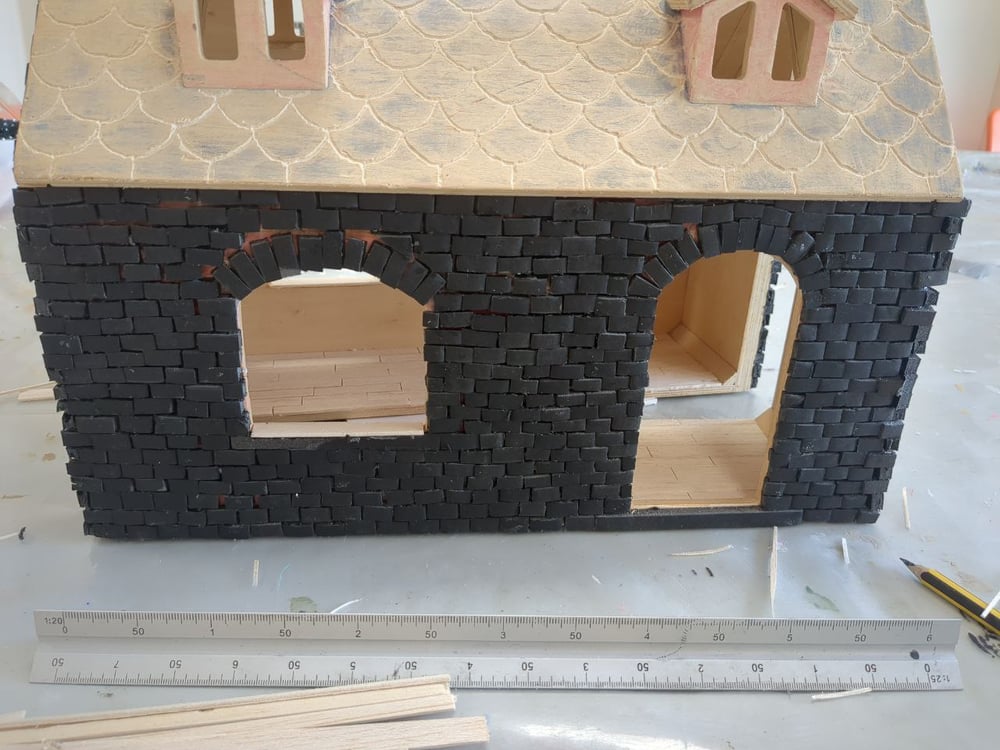 A wooden doll's house with black brickwork glued onto the wall surface.