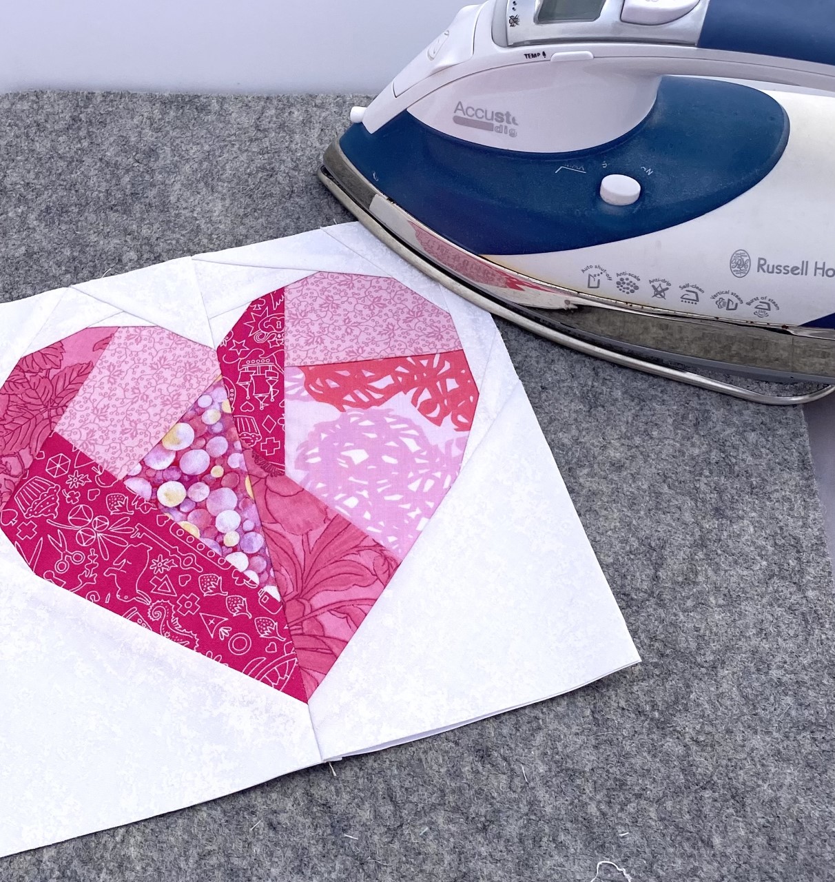 Pressing a paper pieced heart quilt block. Paper pieced geometric heart quilt block being pressed on a wool pressing mat by a Russell Hobbs Iron.