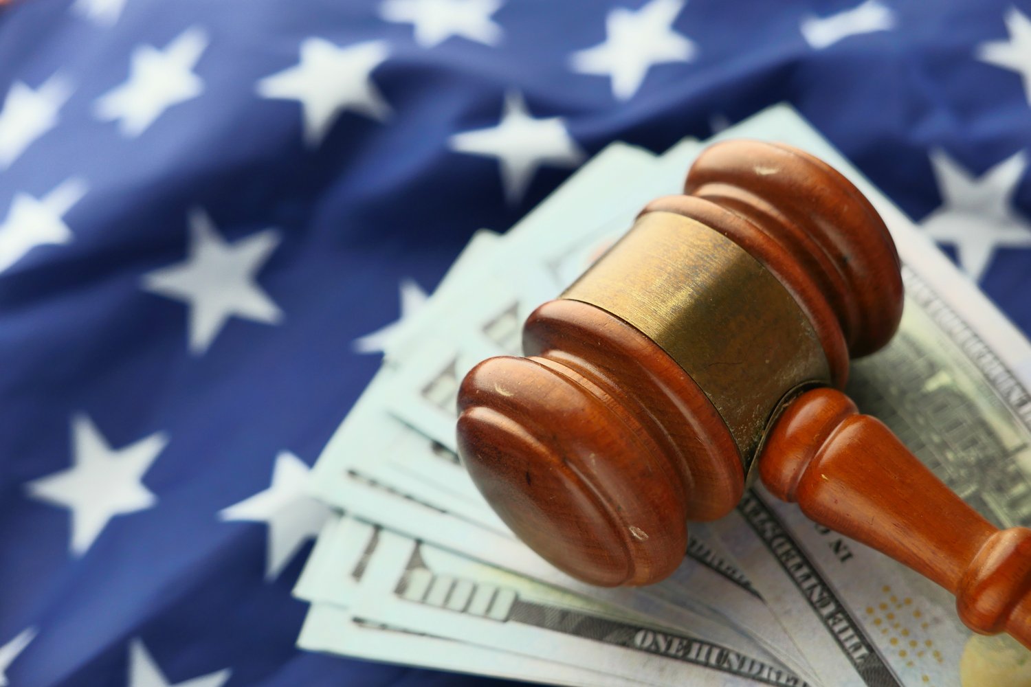 wooden gavel laying on top of hundred dollar bills with American flag in background