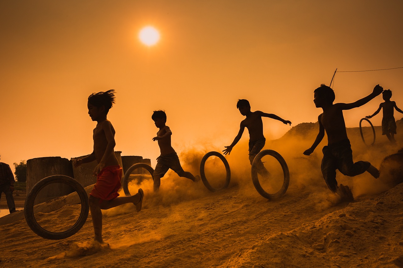 Niños jugando con neumáticos en la arena al calor del sol
