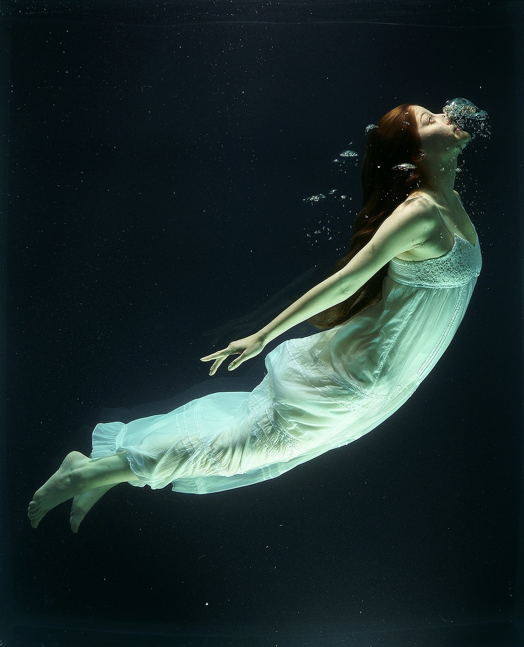Mujer bajo el agua con vestido largo blanco de algodón y cabellera larga, pose de sirena