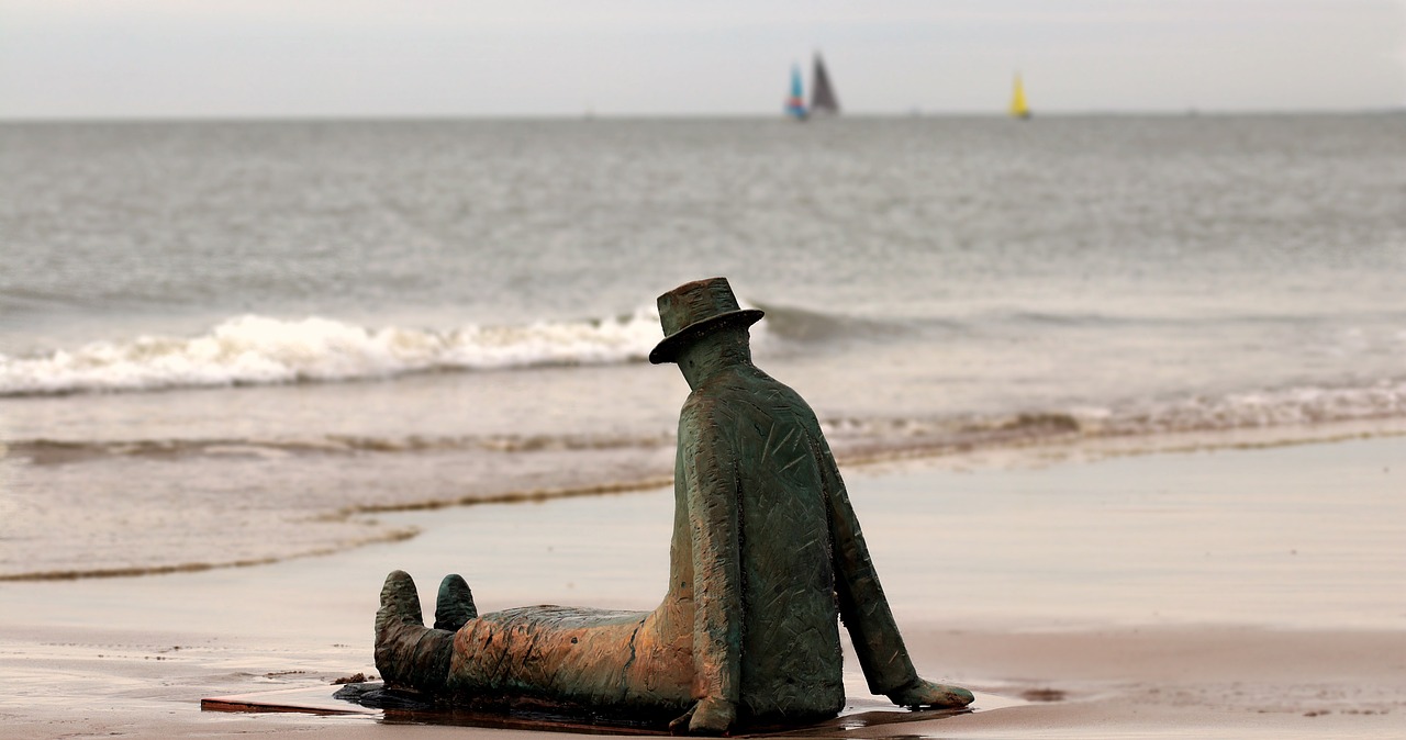 Estatua de hombre con sombrero de bronce sentado frente a la costa belga