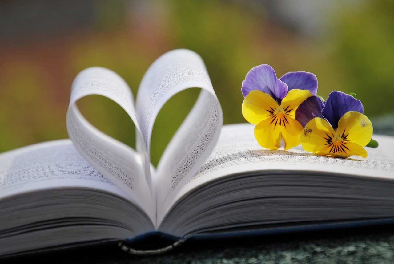 Libro abierto, hojas en forma de corazón, flores lilas y amarillas