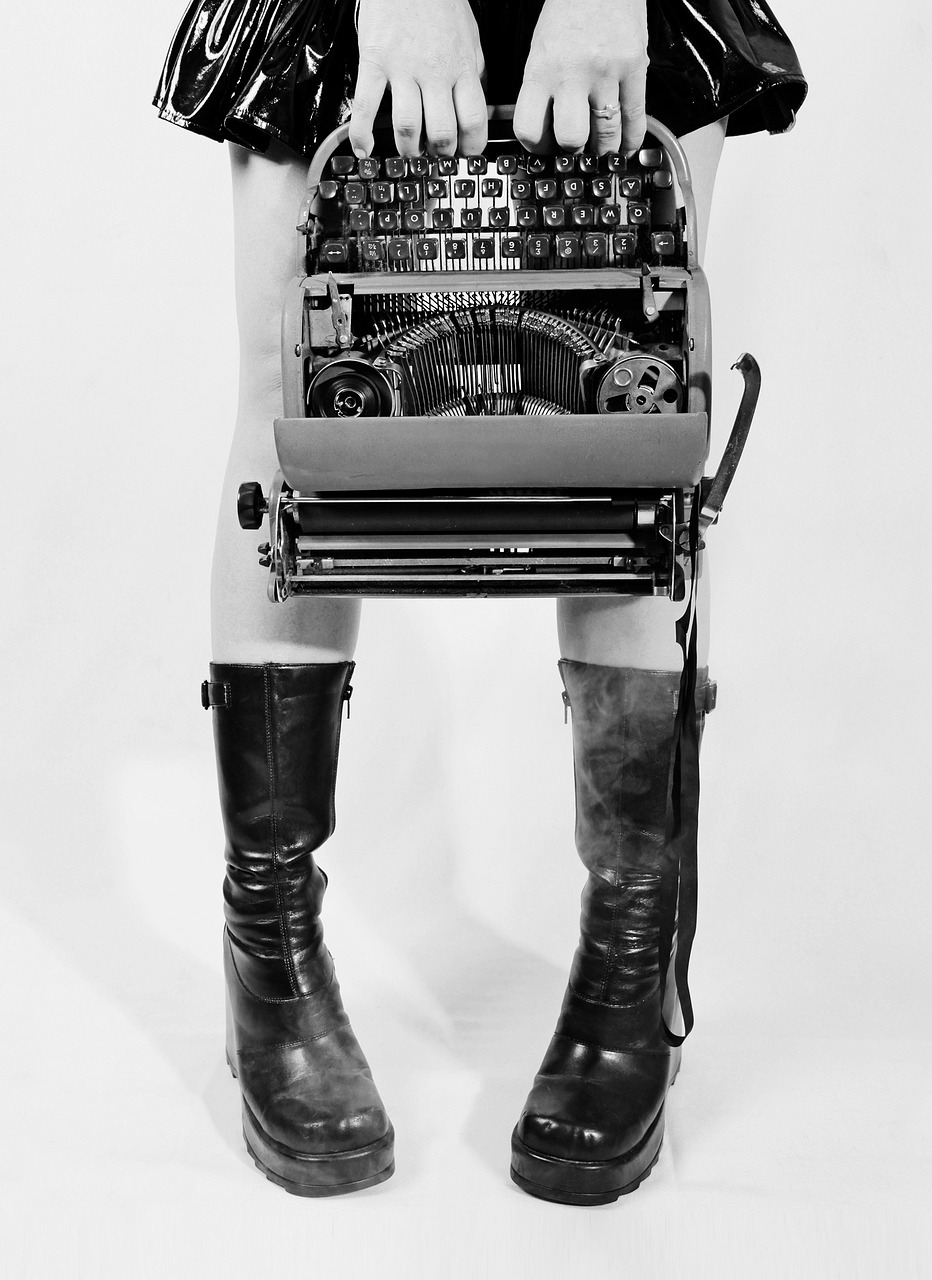 Foto en blanco y negro de máquina de escribir, y chica con falda y botas negras sujetándola