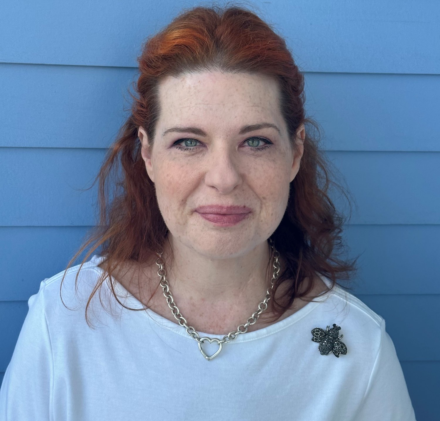 margo smiling wearing a white shirt with a bee broach infront of a blue background