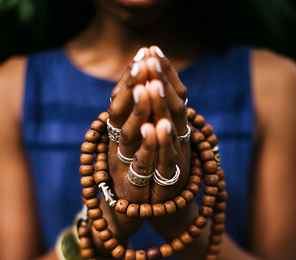 close up afro american womans hands with a mala bead necklace wrapped around them
