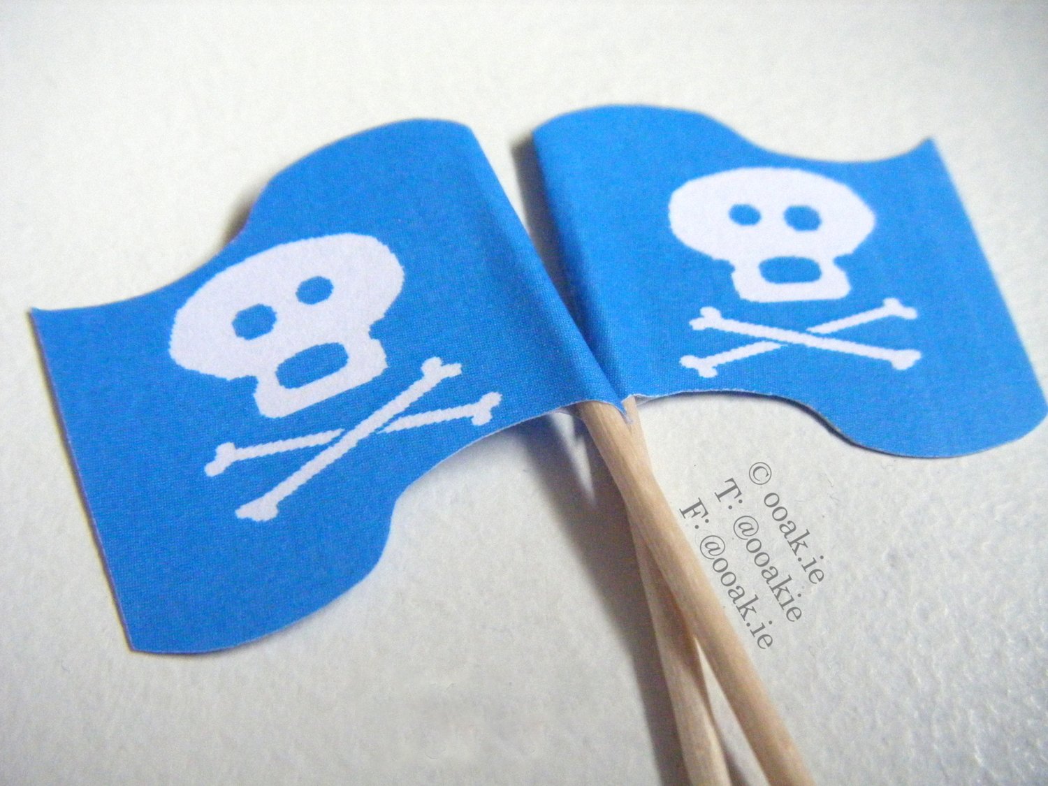 close up of 2 jolly roger flags, white skull and crossbones on a blue wavy flag.
