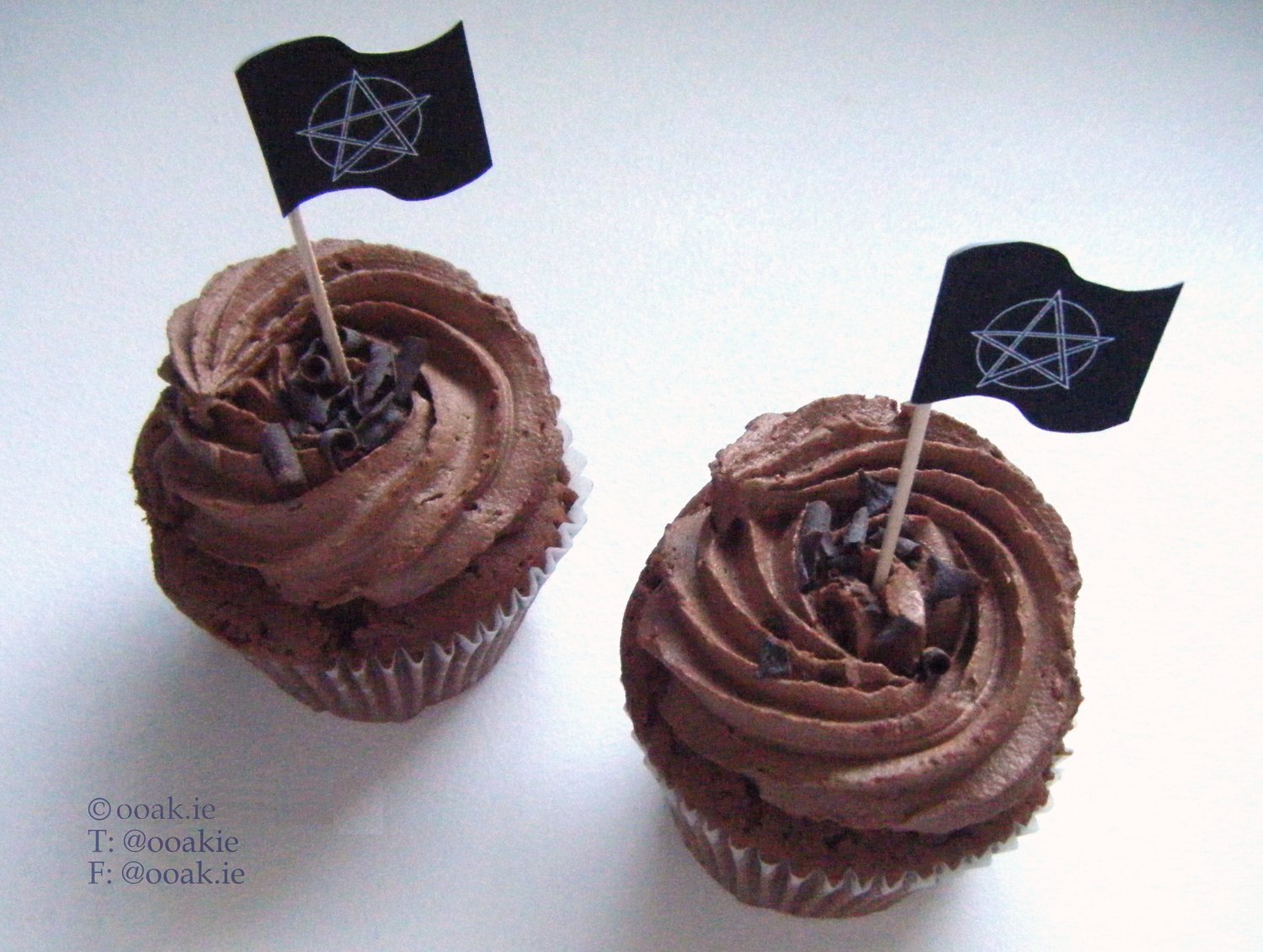 Two chocolate cupcakes with flag toppers - the flags show a pentacle on front of an outline of the moon