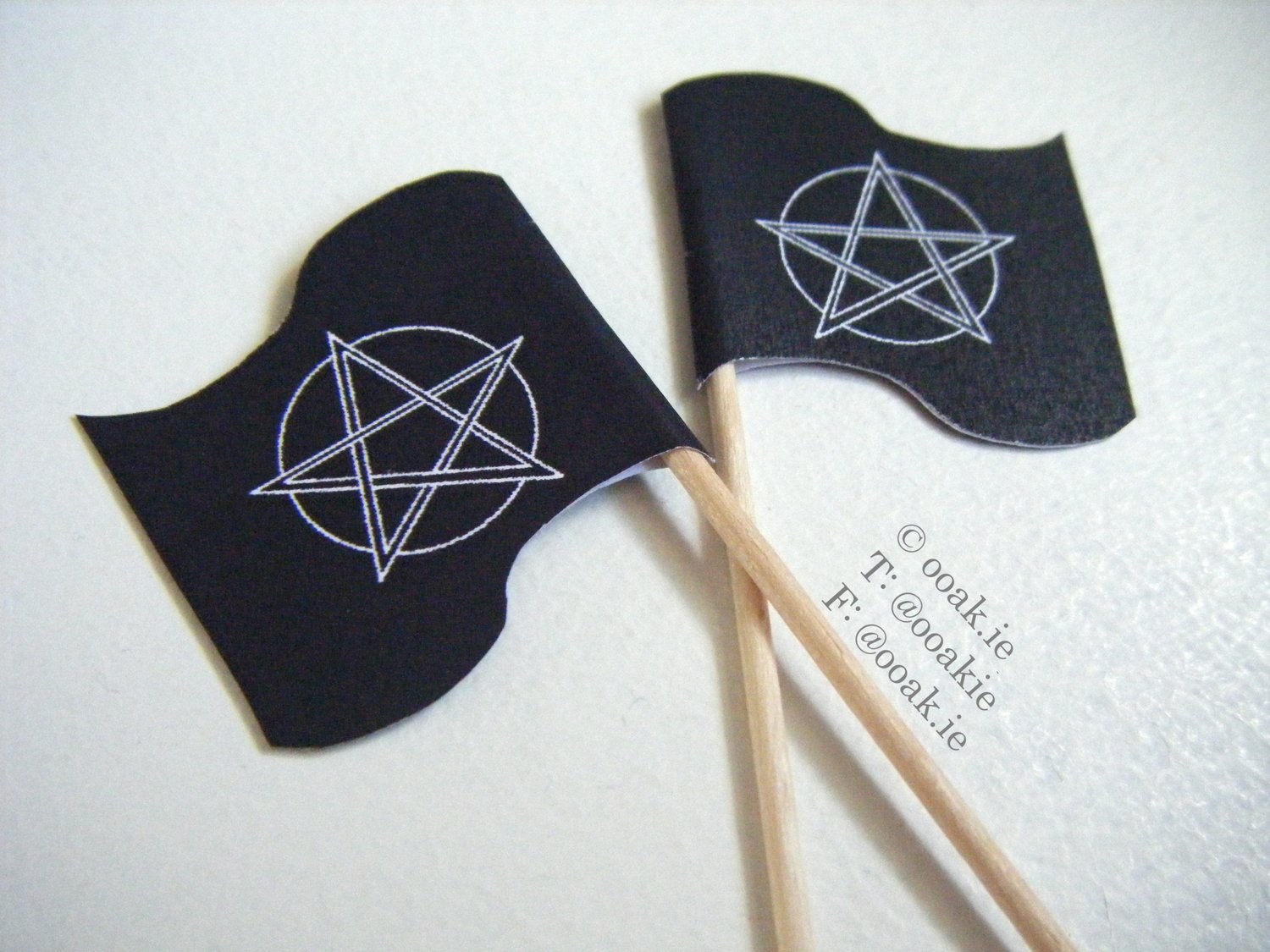a close-up of two cocktail stick flags. The flags show a white pentacle on front of an outline of the moon on a black background