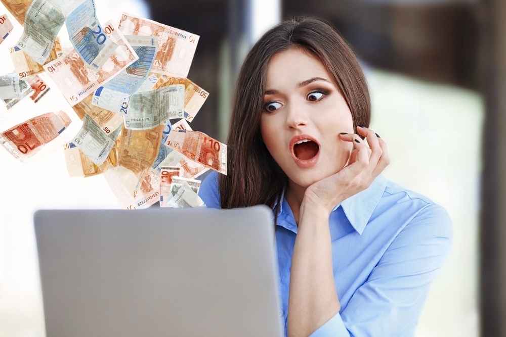 the woman is sitting in amazement at the laptop, from which money is flying out