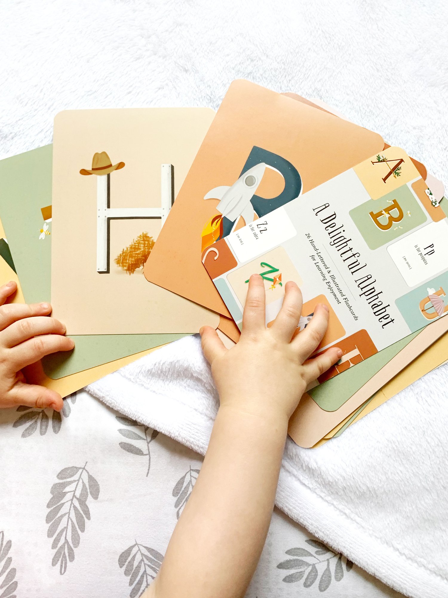 Toddler hands touching set of bright and whimsical alphabet flash cards for girls or boys