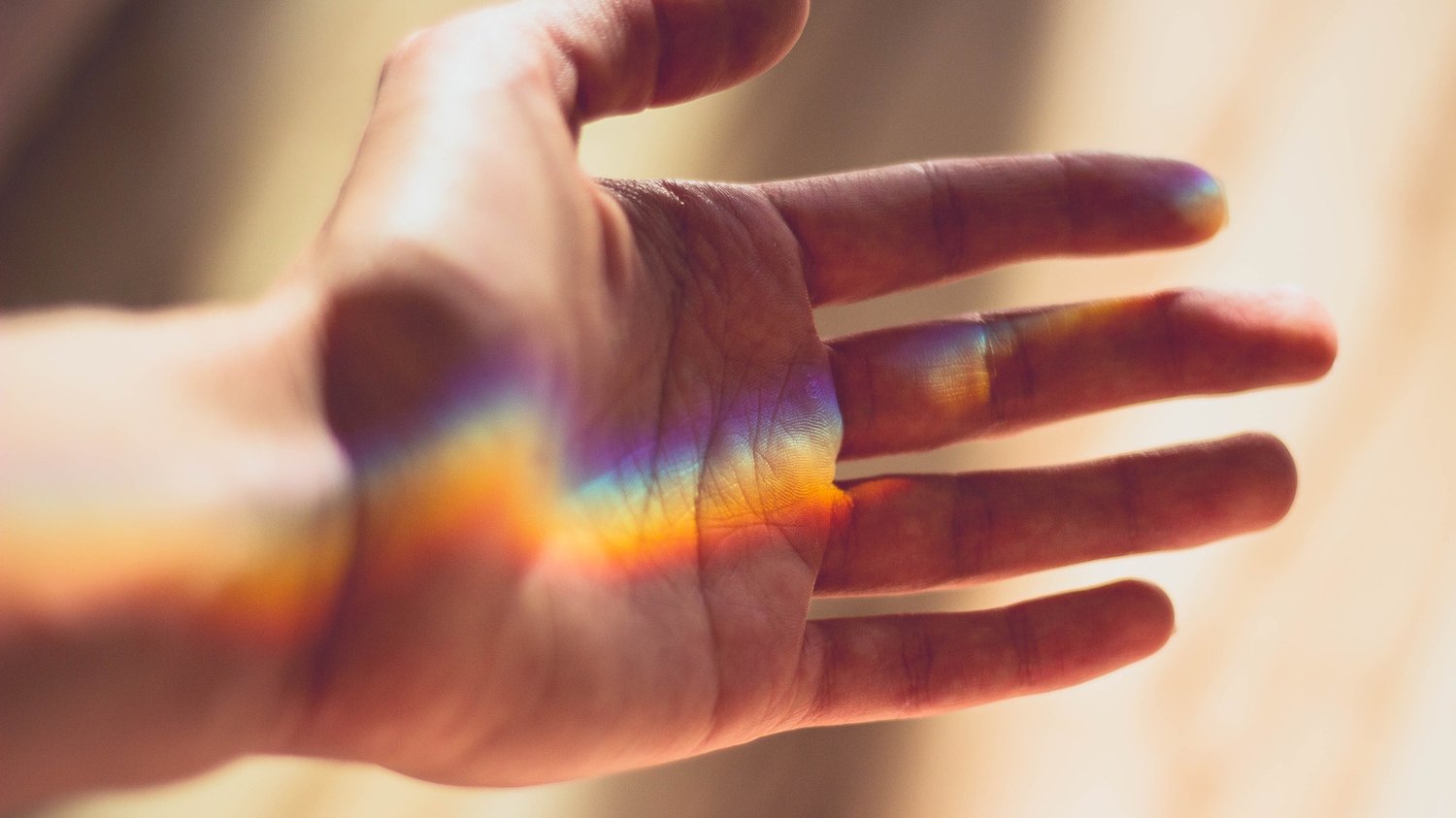 Image of outstretched hand with diffracted rainbow colours falling across it