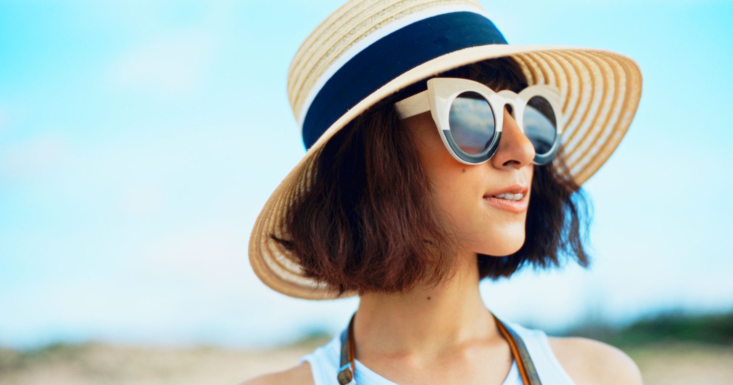A woman in a sun hat on the beach has perfect complexion.