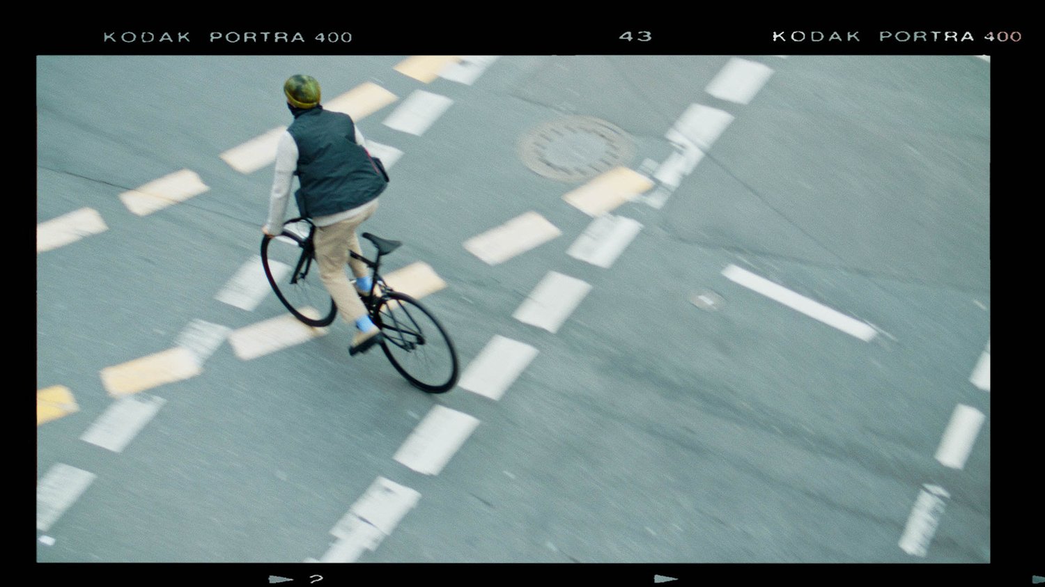 A man peddles his bike quickly across a street intersection painted with lines.