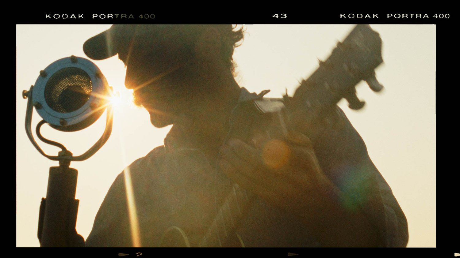 A man in a baseball cap plays the guitar at sunset.