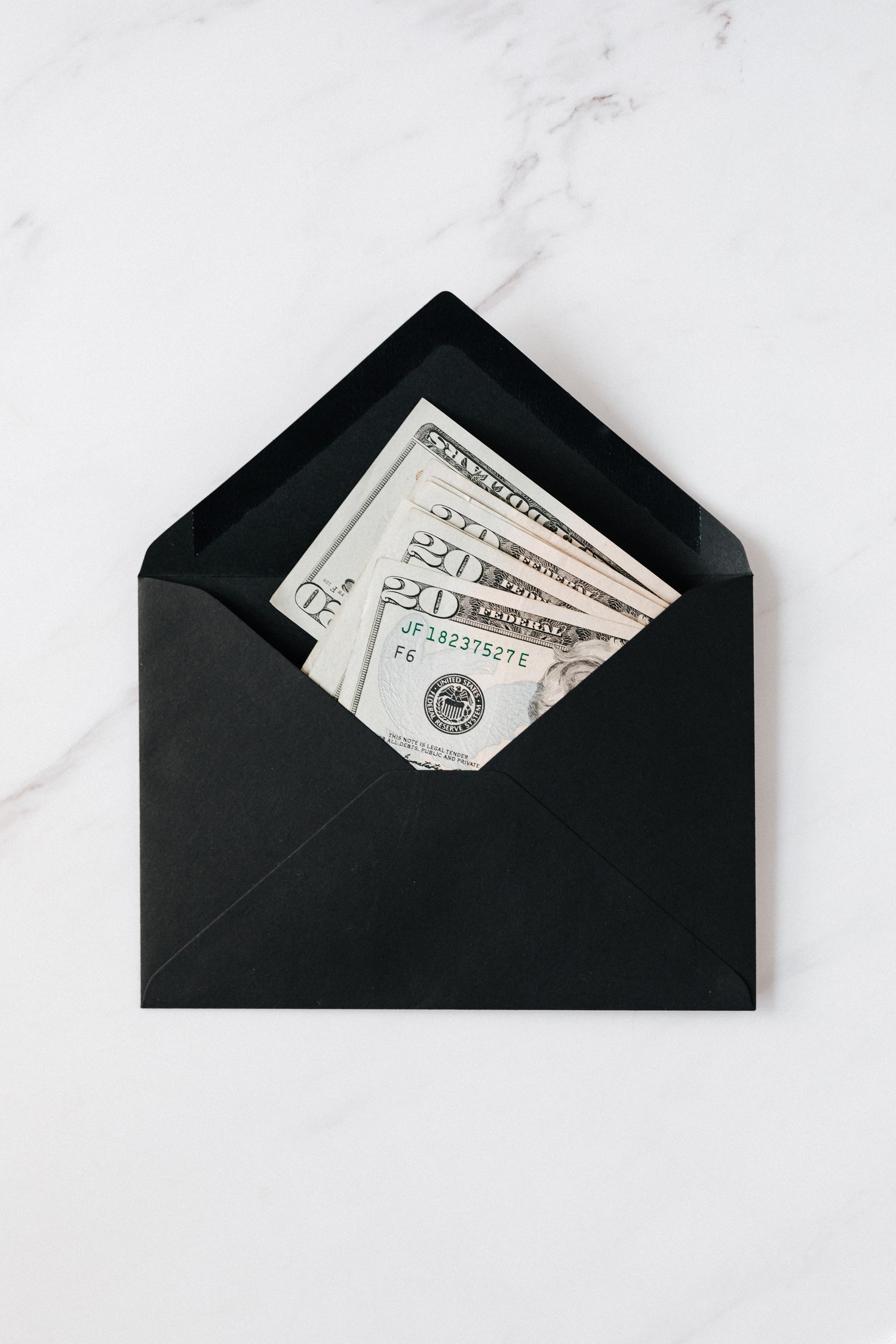 Black envelope with $20 bills on marble background | The Musicpreneur Model for self-employed musicians and music freelancers by Ashley Danyew & Steve Danyew