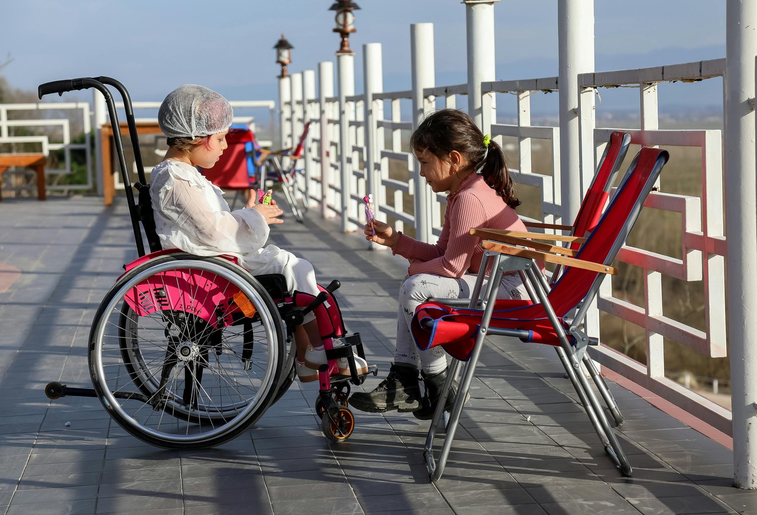 two little girls, one in her wheelchair, talking on a sunny boardwalk