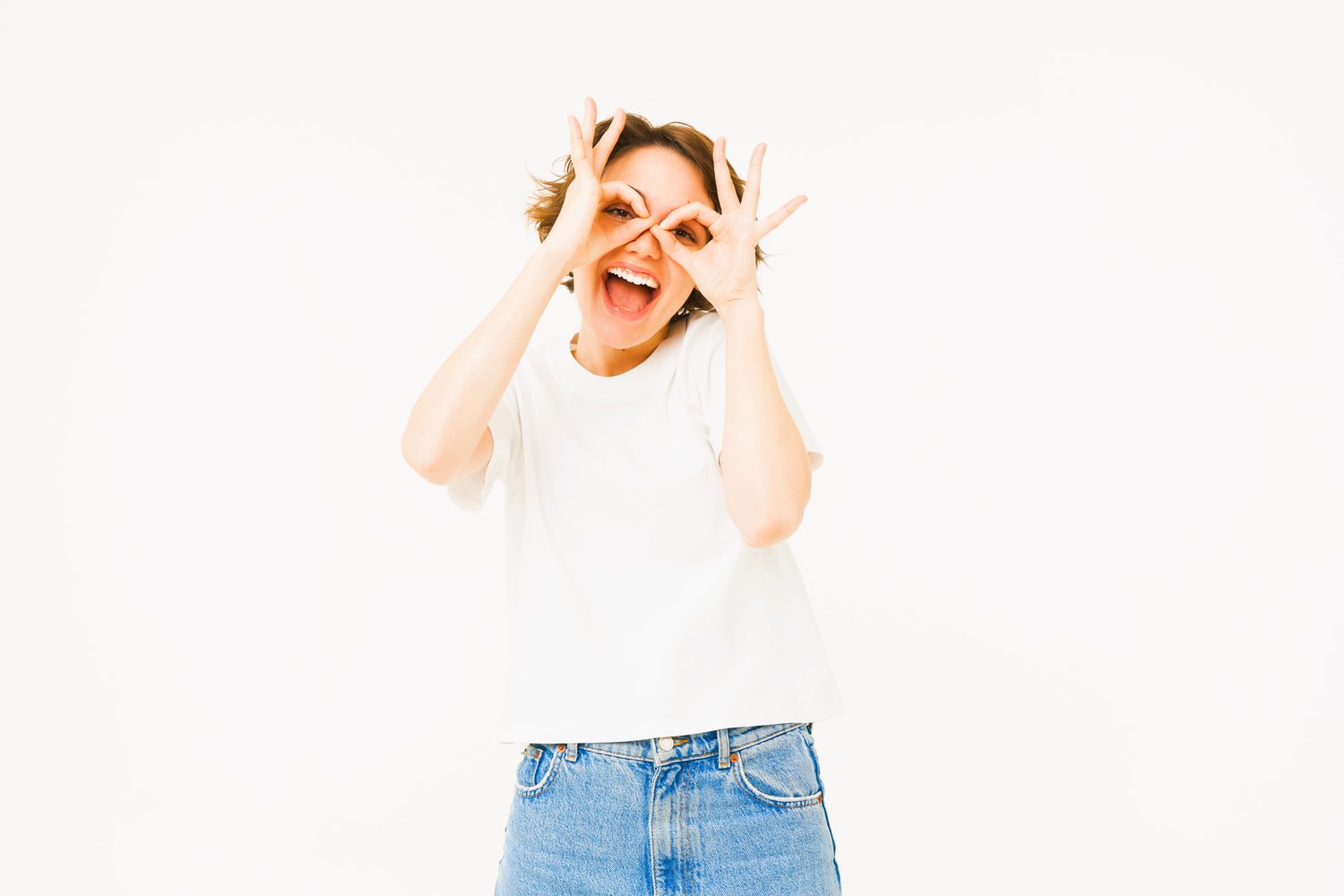 Retrato de una mujer despreocupada mostrando gafas con las manos sobre los ojos y sonriendo, posando