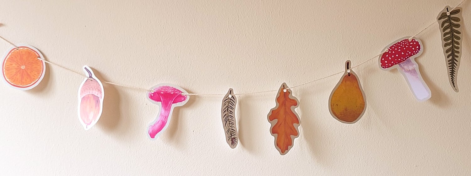 8 cut out paper illustrations of leaves, fruit and mushrooms hanging on a wall on string