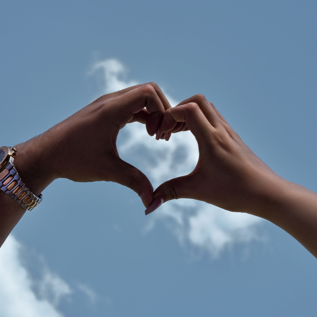 Hands forming a heart against a blue sky, symbolizing love, connection, and the importance of self-care and emotional well-being.