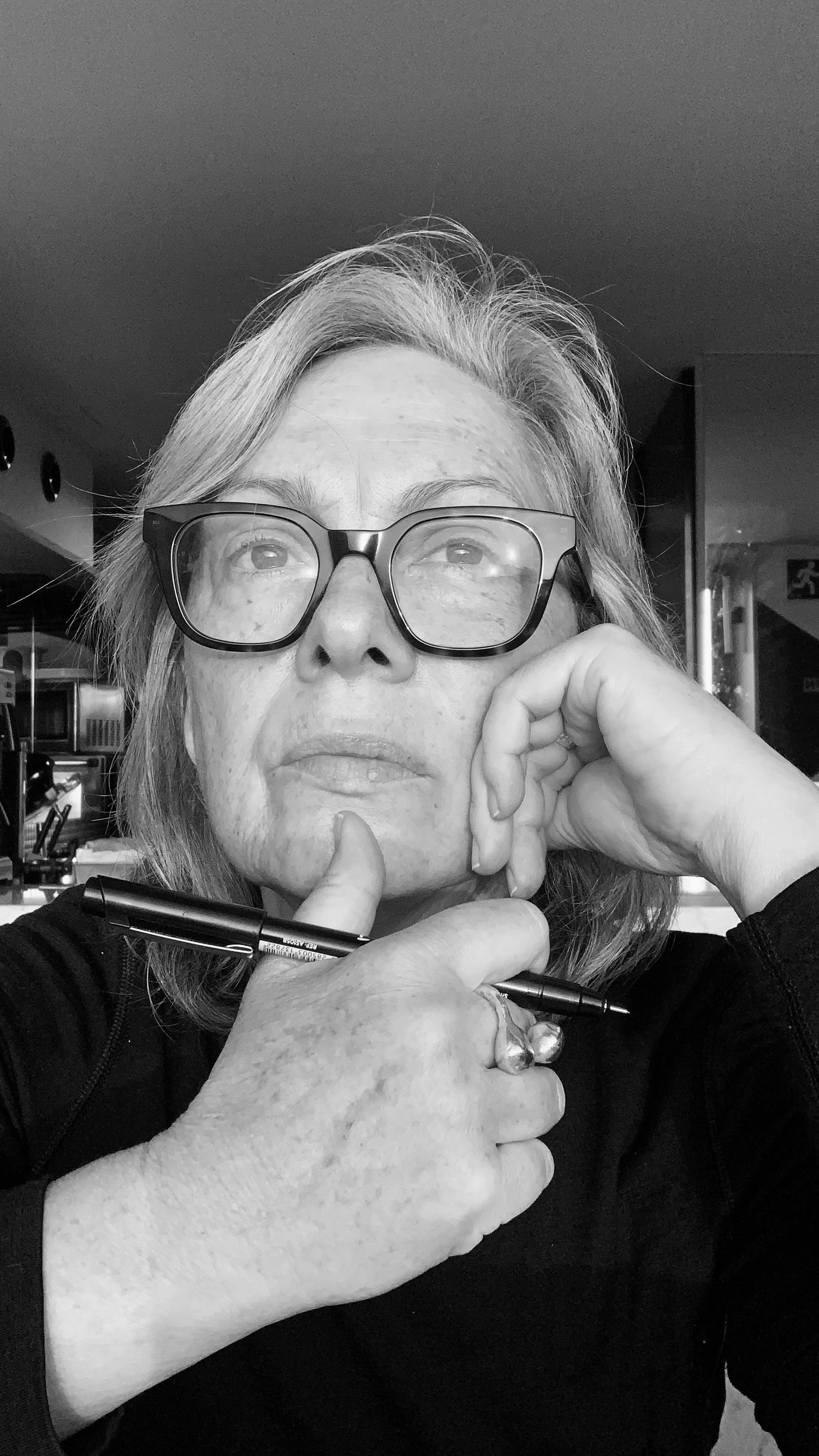 A black & white head shot of a woman looking out contemplating with a pen in her hand ready to write.