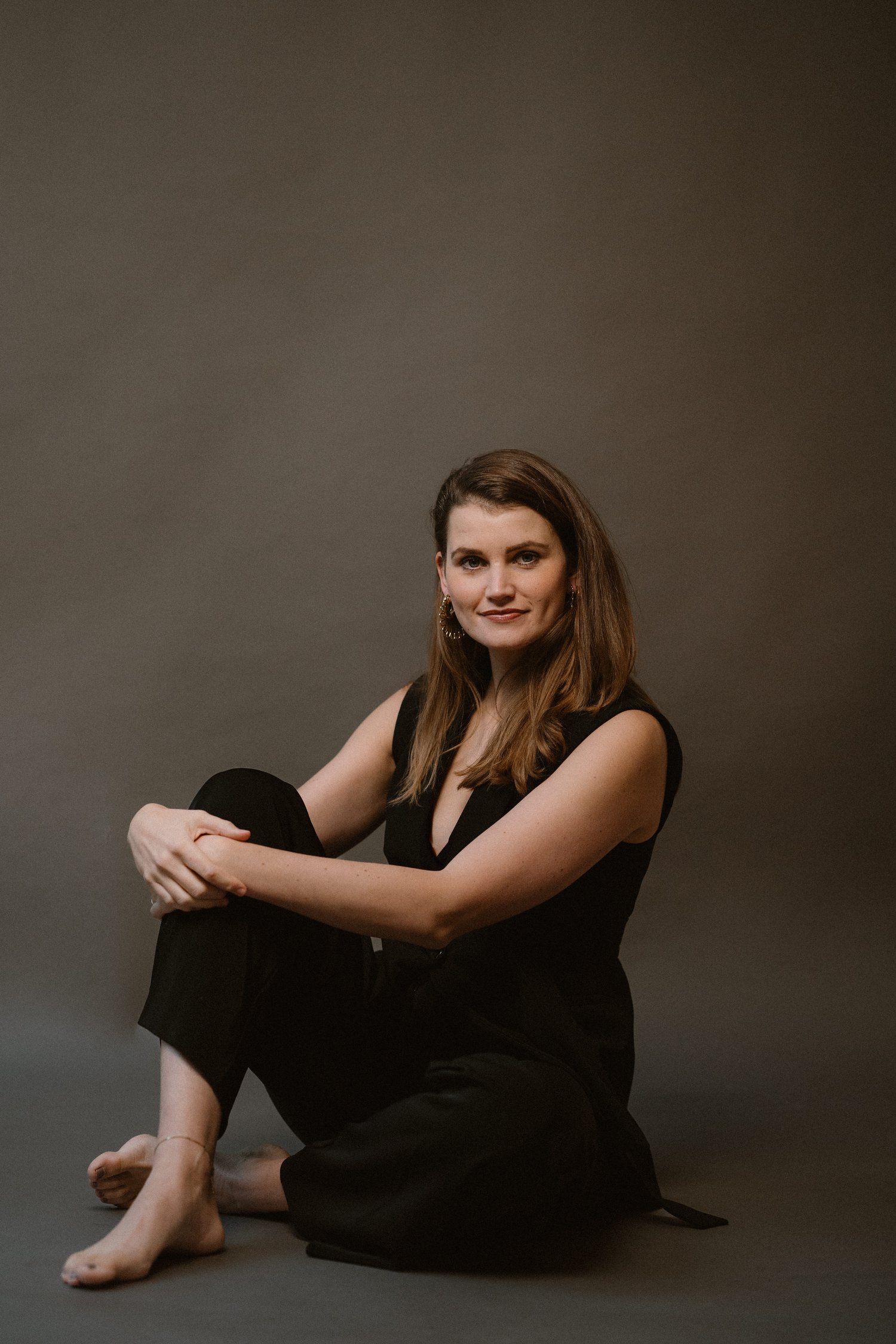 Fleur Bruin coach in black suit sitting on the ground with a soft smile looking into the camera