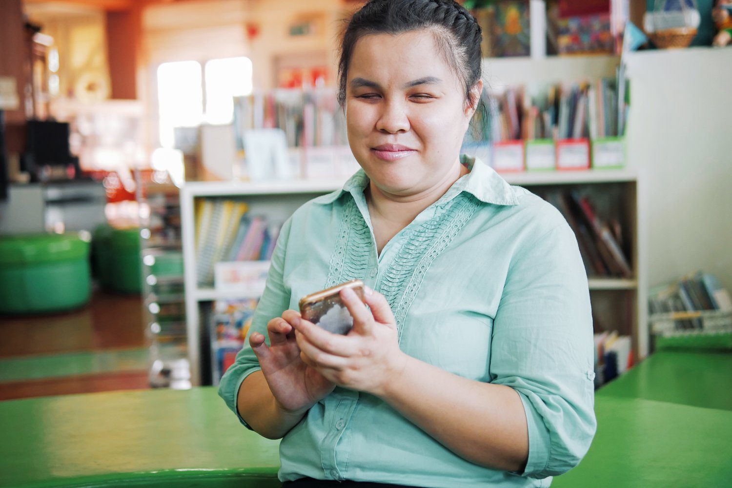 smirking blind woman in a blue shirt tapping at her mobile phone screen