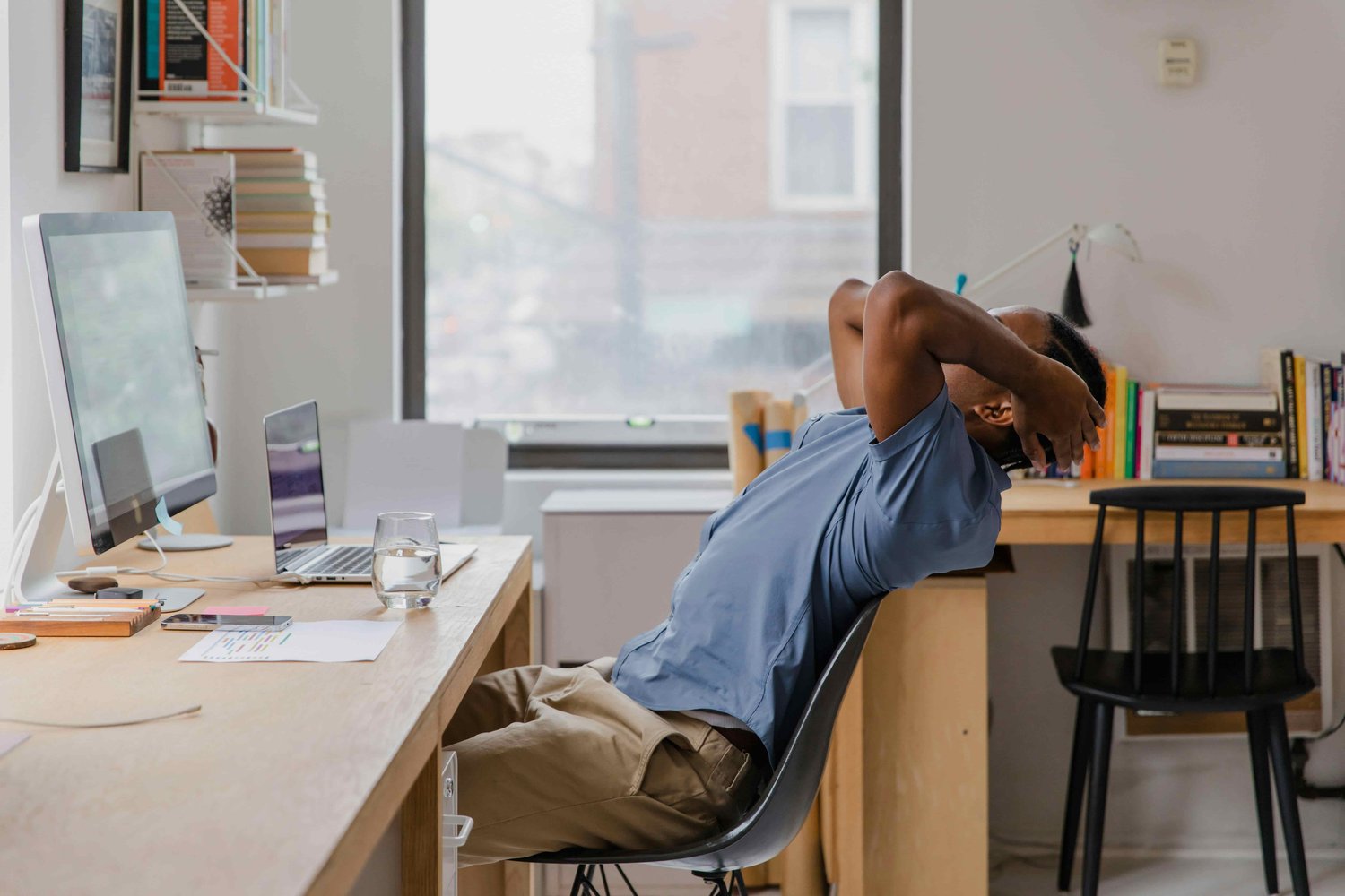 a man leaning his head into his hands stretching his back over his chair