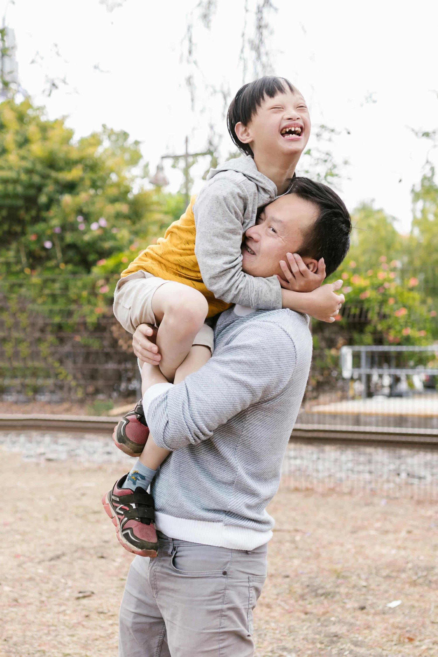 an Asian father holding his smiling, neurodivergent little boy