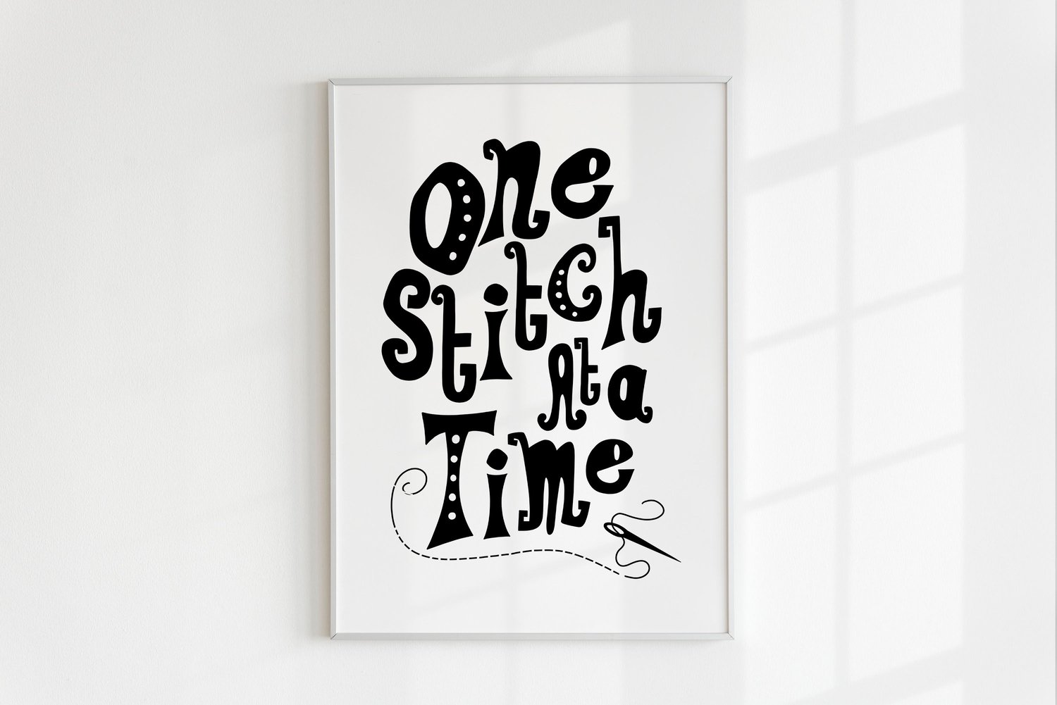 A downloadable print with a hand lettered design which says ‘one stitch at a time’ in black.
