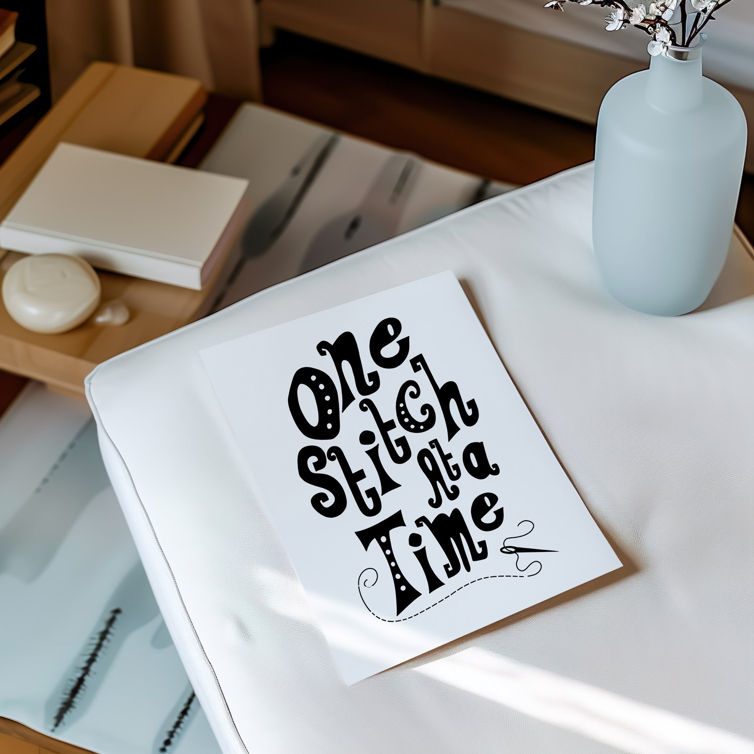 A downloadable print with a hand lettered design which says ‘one stitch at a time’ in black.