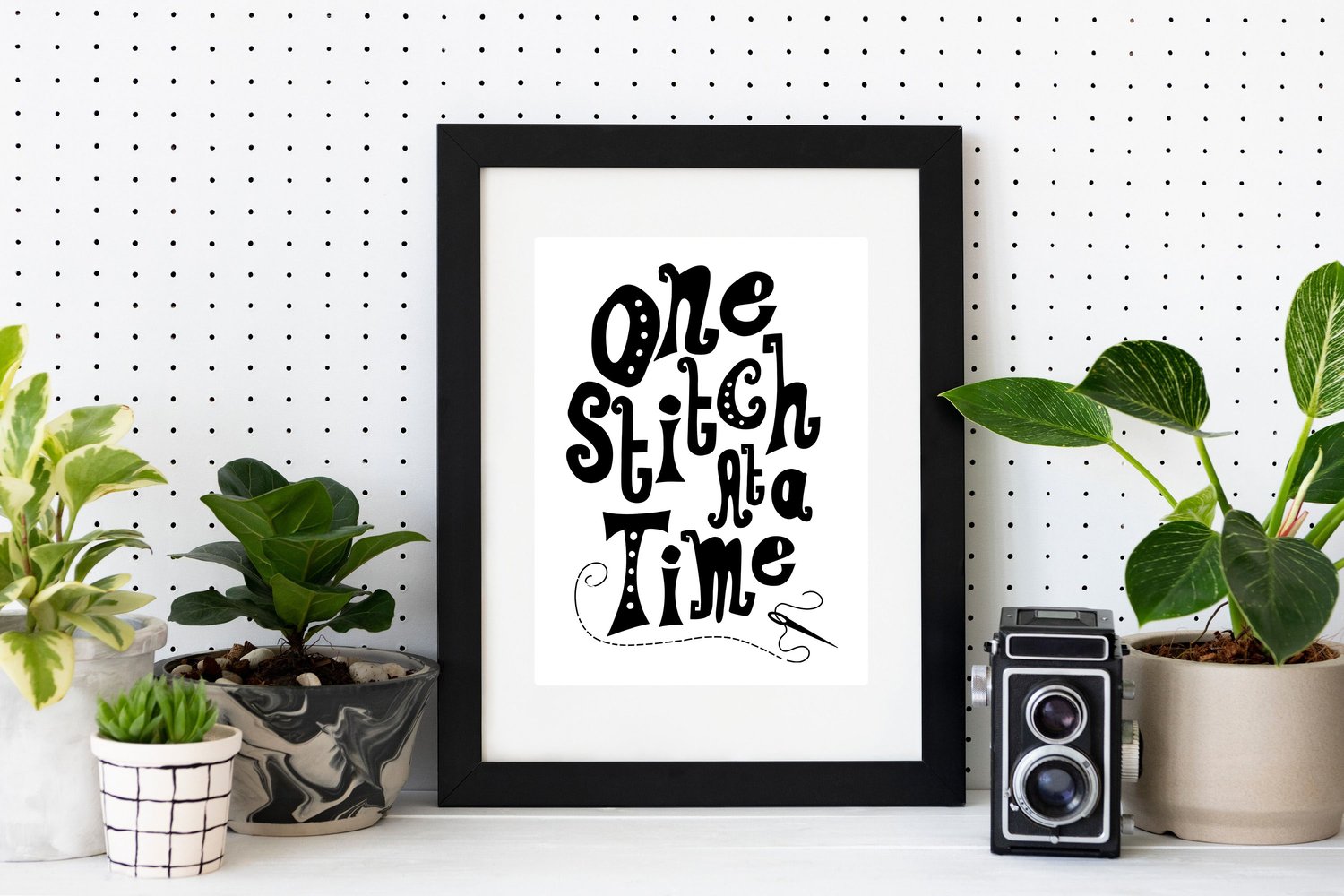 A downloadable print with a hand lettered design which says ‘one stitch at a time’ in black.