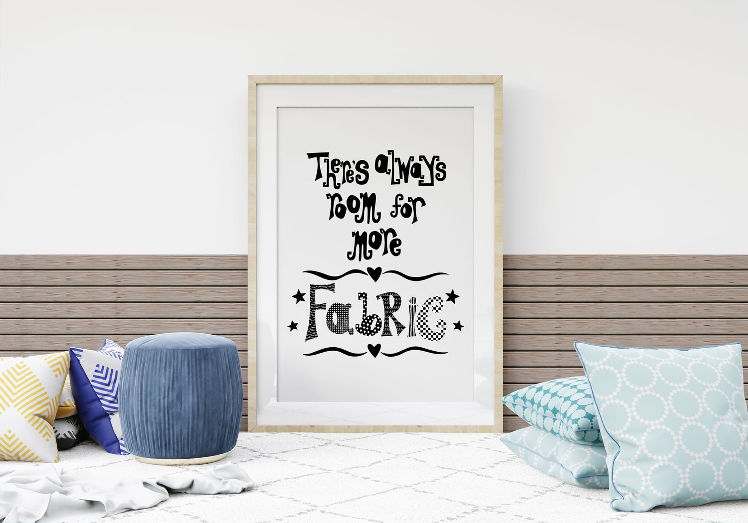 A downloadable print with a hand lettered design which says ‘there’s always room for more fabric’ in black. This example is framed in a light wooden frame and resting against the wall with some scatter cushions.