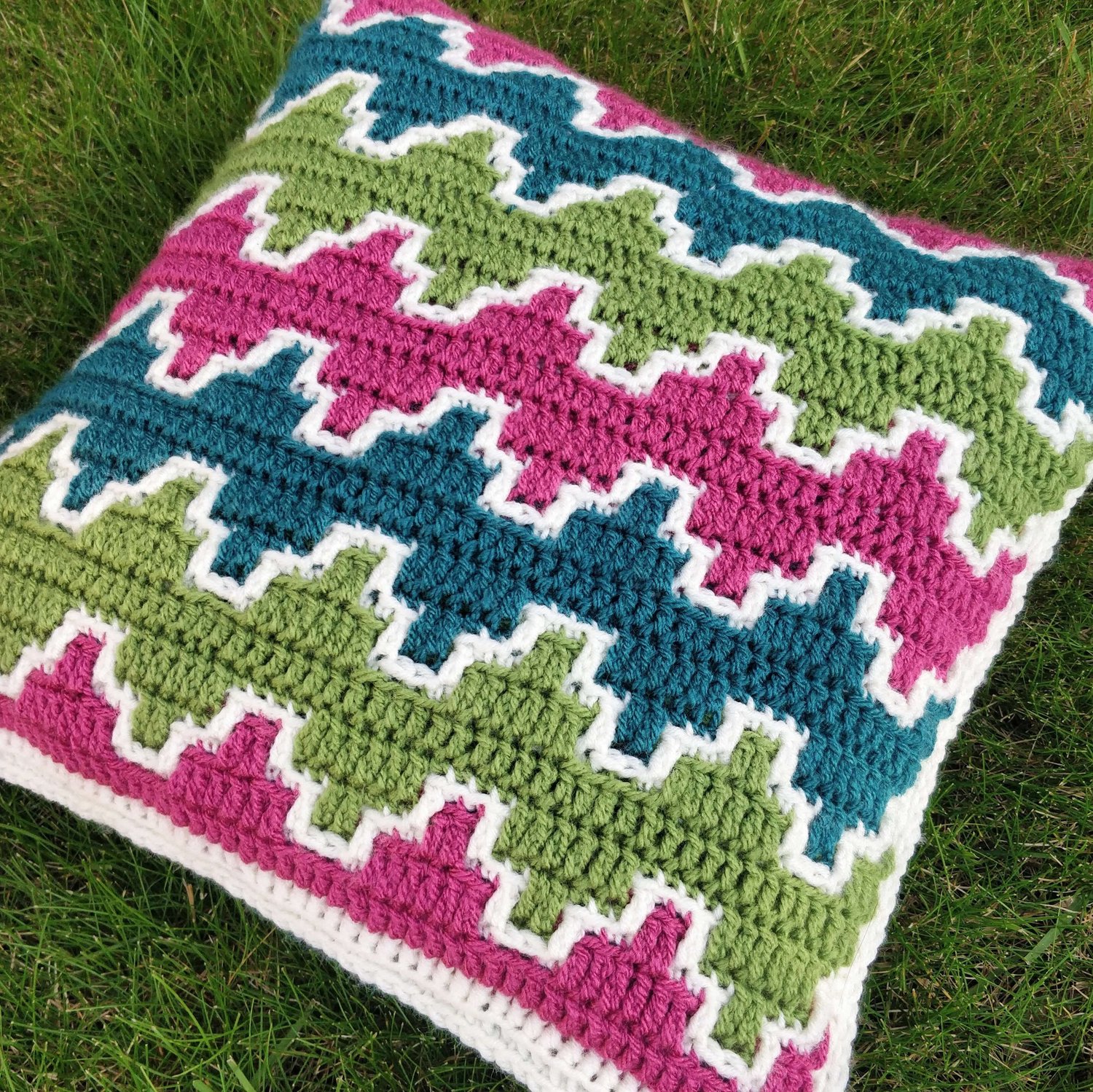 A crocheted cushion with pink green and teal zig zags across it