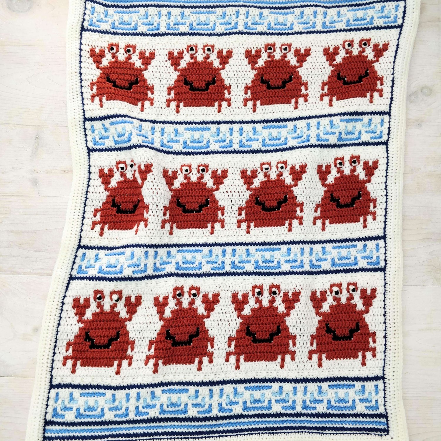 Orange crabs arranged in rows with blue waves in between as a crochet blanket