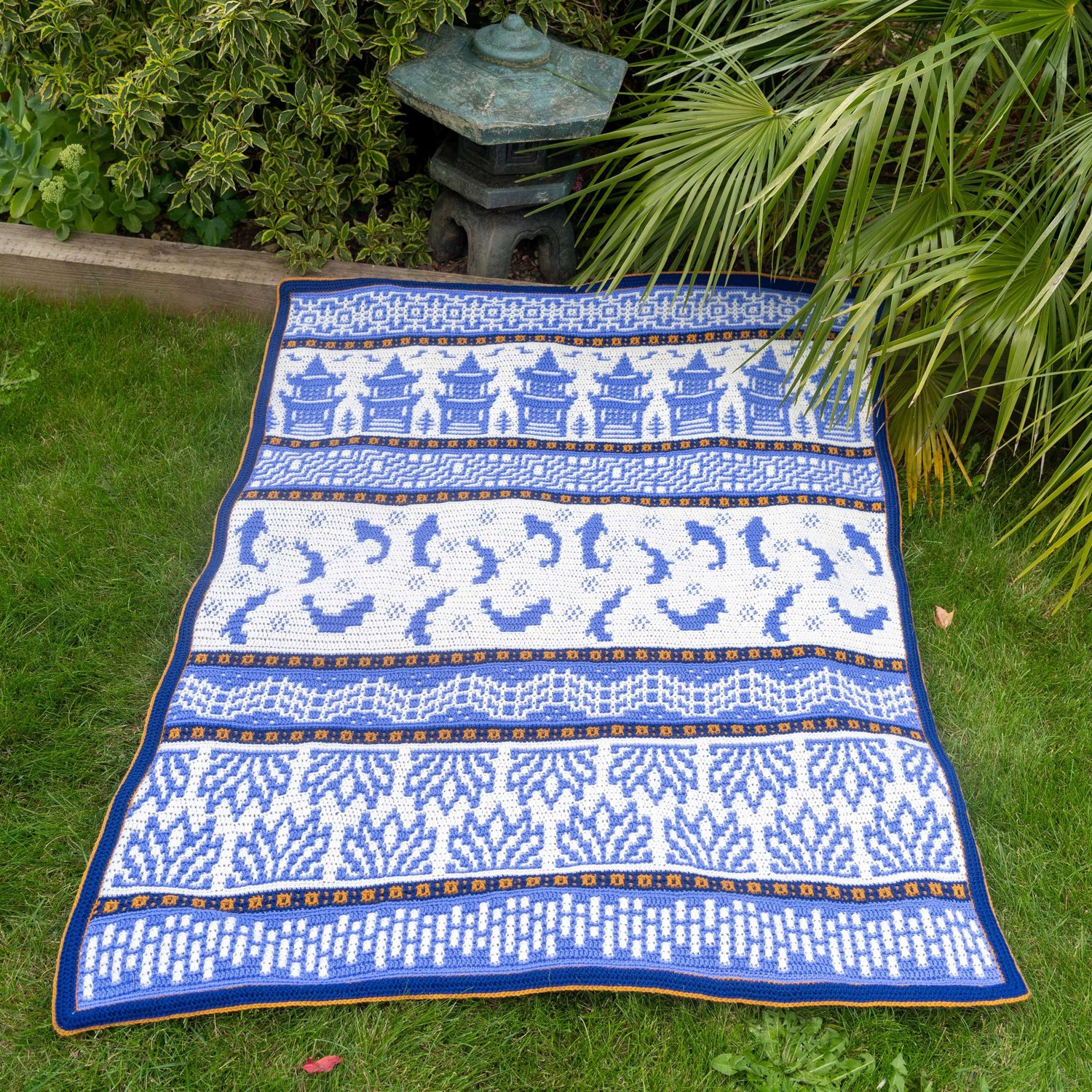 Blue and white blanket showing Japanese symbols of stones lotus bridge fish trellis tea houses on a lawm