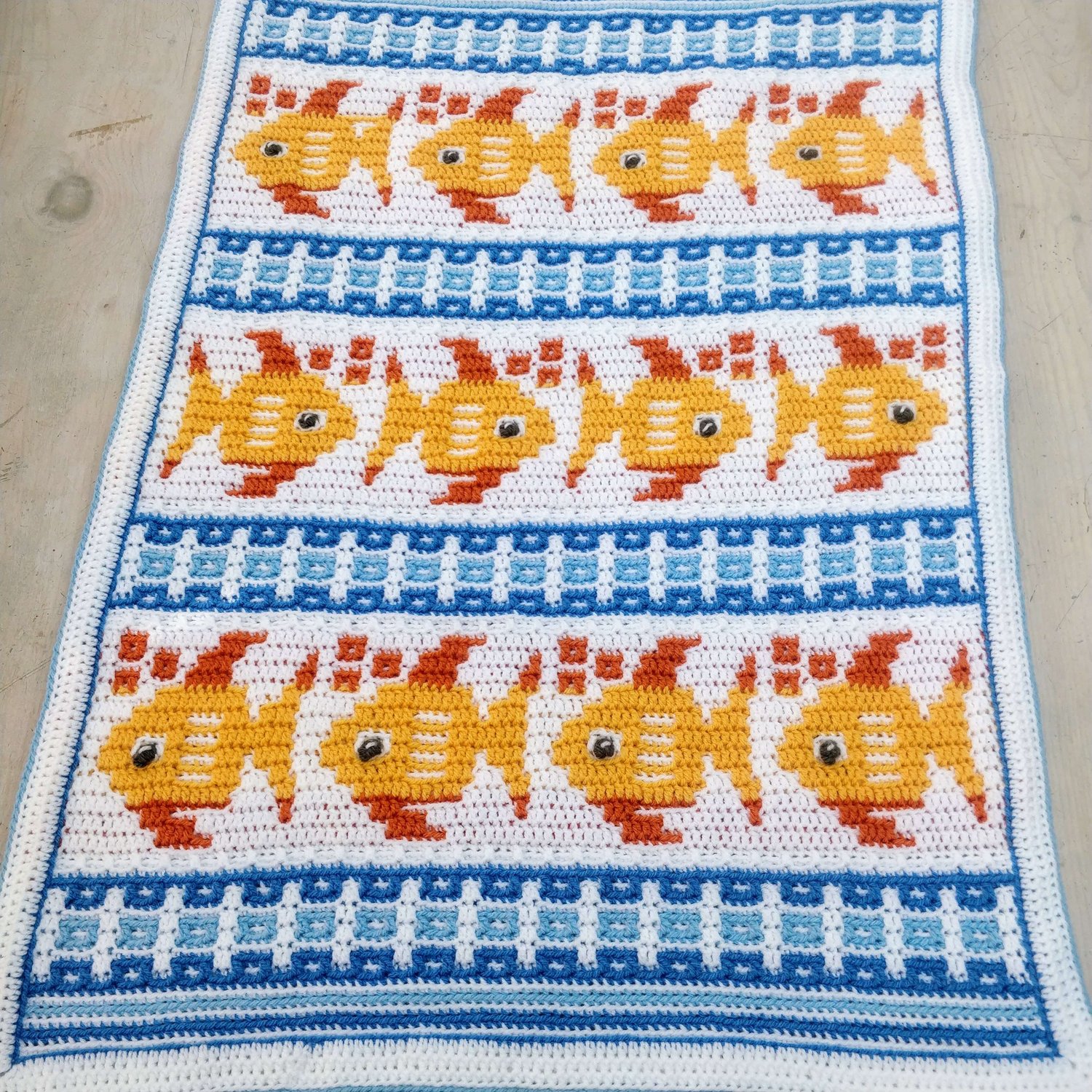 Crochet blanket showing cute gold fish arranged in rows with blue waves in between