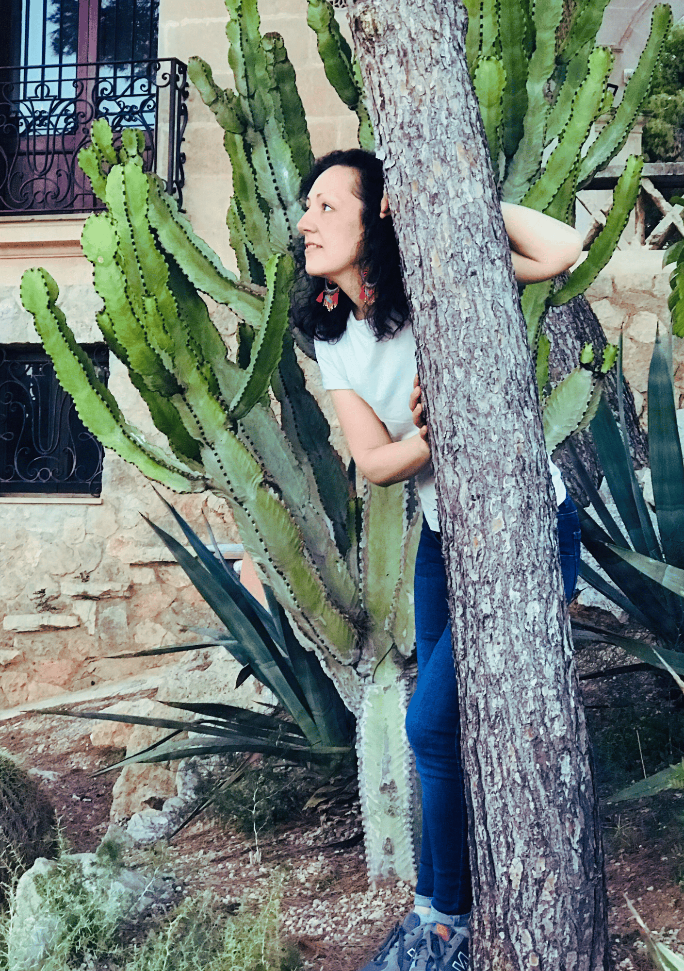Isabel Bar playfully peeking from behind a tree next to a tall cactus, smiling — About page on iamisabelbar.com