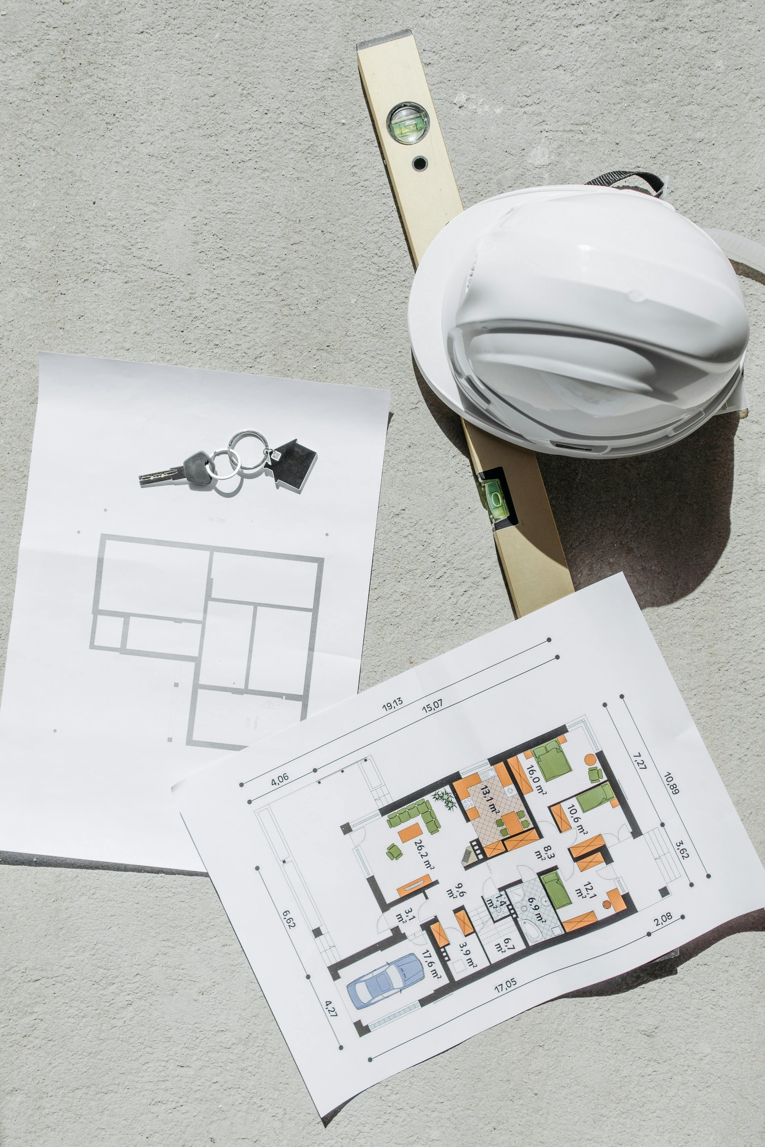 Image of a hardhat, blueprints, keys and level on a table