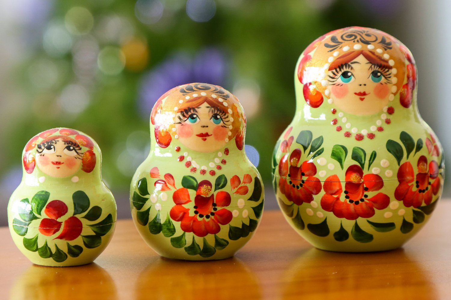 Three hand painted Russian Dolls decorated with red flowers and green petals with bright blue eyes