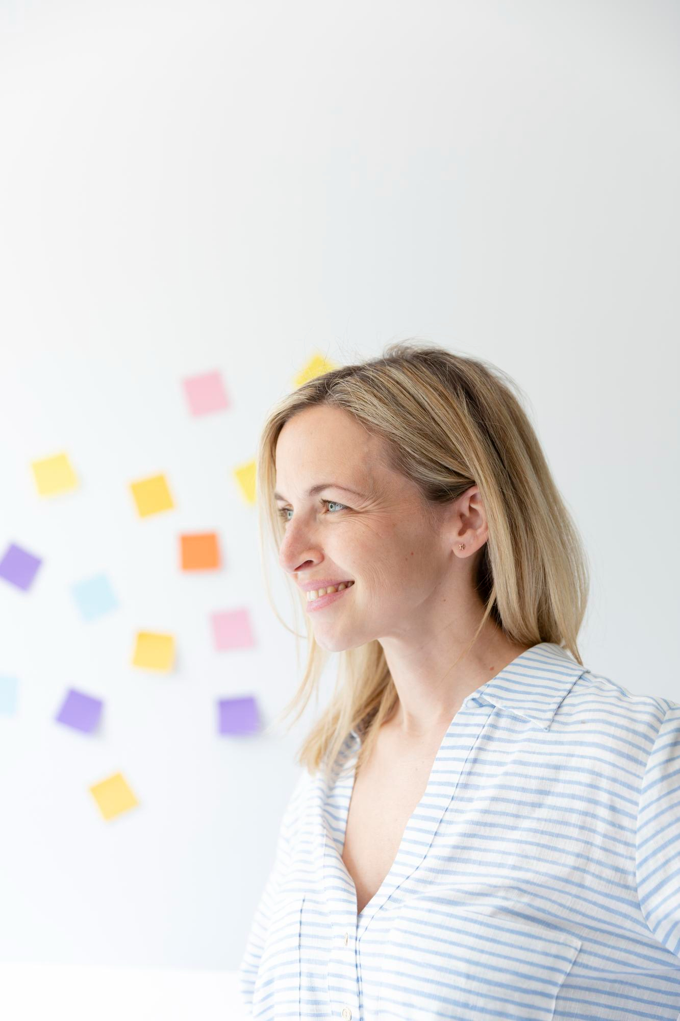 Portrait d'une jolie jeune femme blonde avec un beau sourire devant un mur blanc avec des notes autocollantes colorées et est une personne heureuse