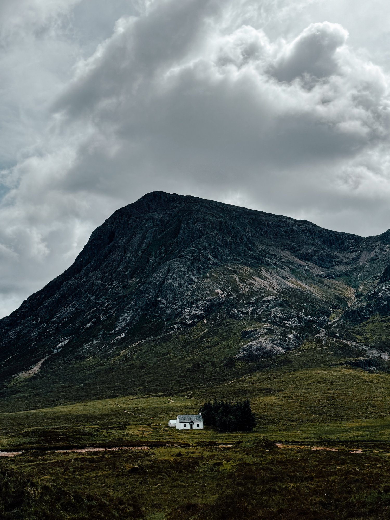 a white house sits in a green field with mountains surrounding it in the Scottish Highlands
